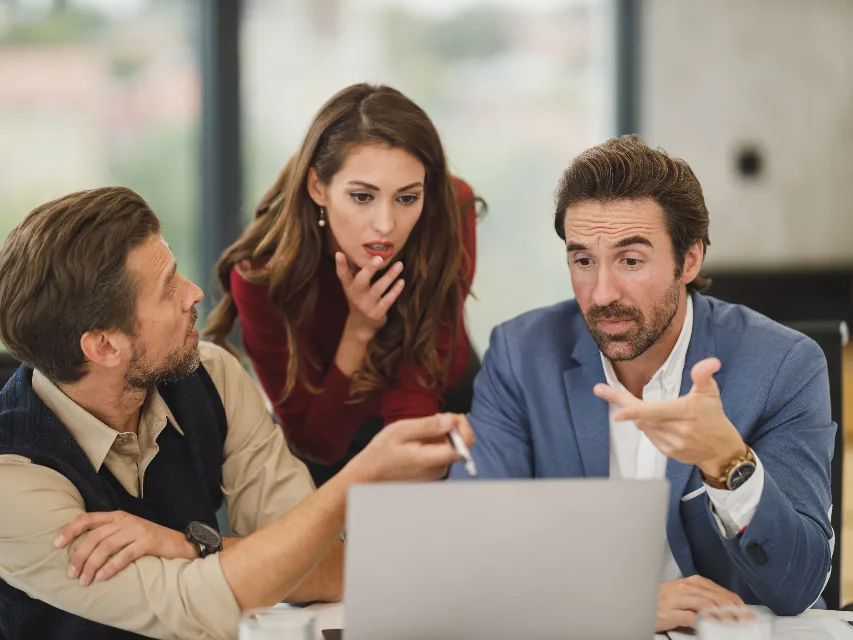Three colleagues discussing figures on a laptop