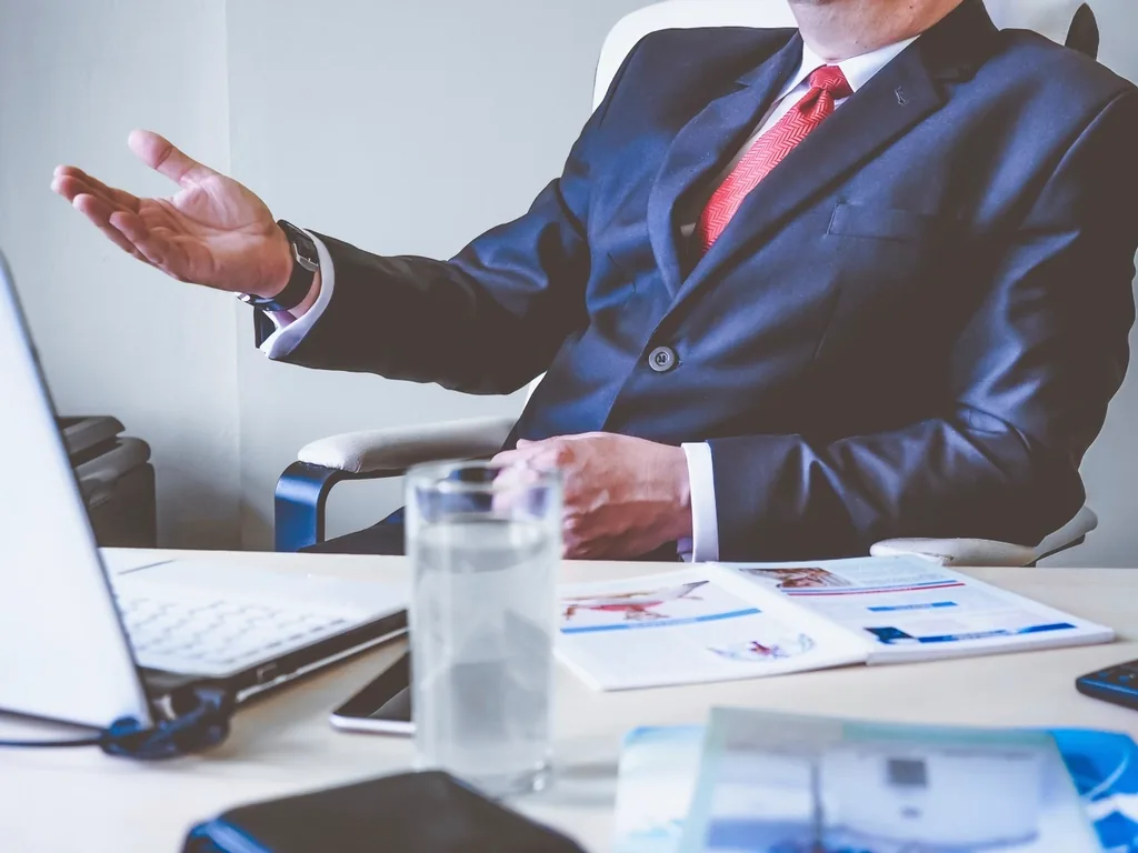 An advisor in a suit talking across a desk covered with documents and a laptop